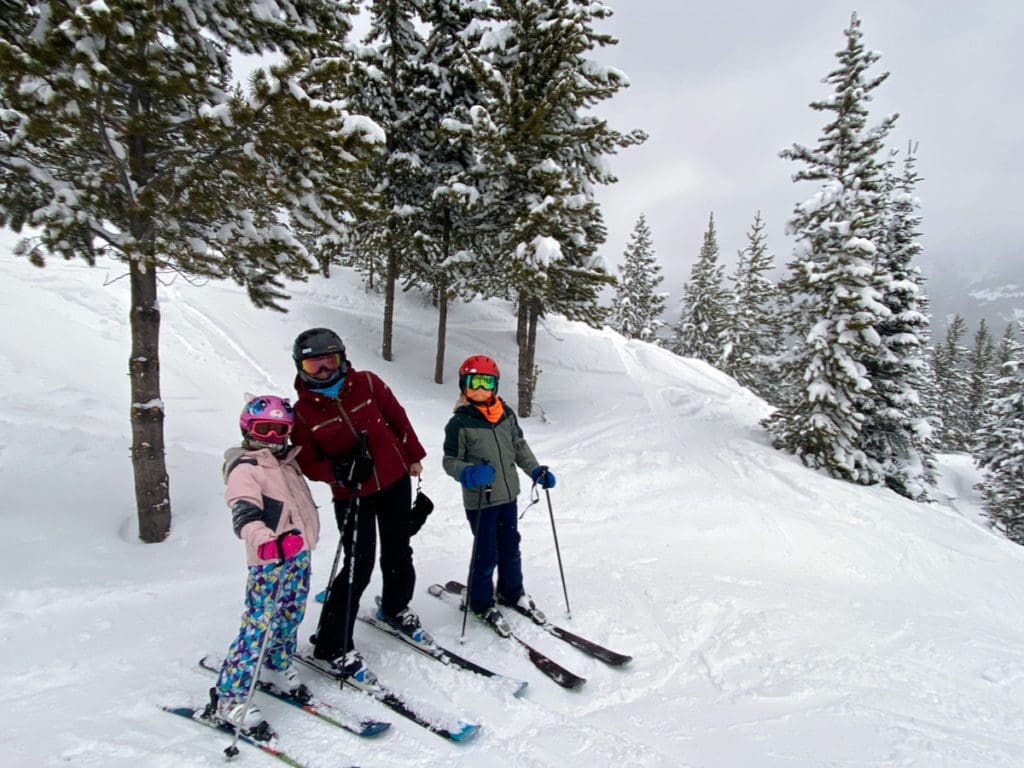 A mom and her two kids stand together, while on skis, at Big Sky.