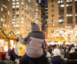 A young child sits atop the shoulder of an adult to take in a view of the lights and market sights at Christkindlmarket Chicago.