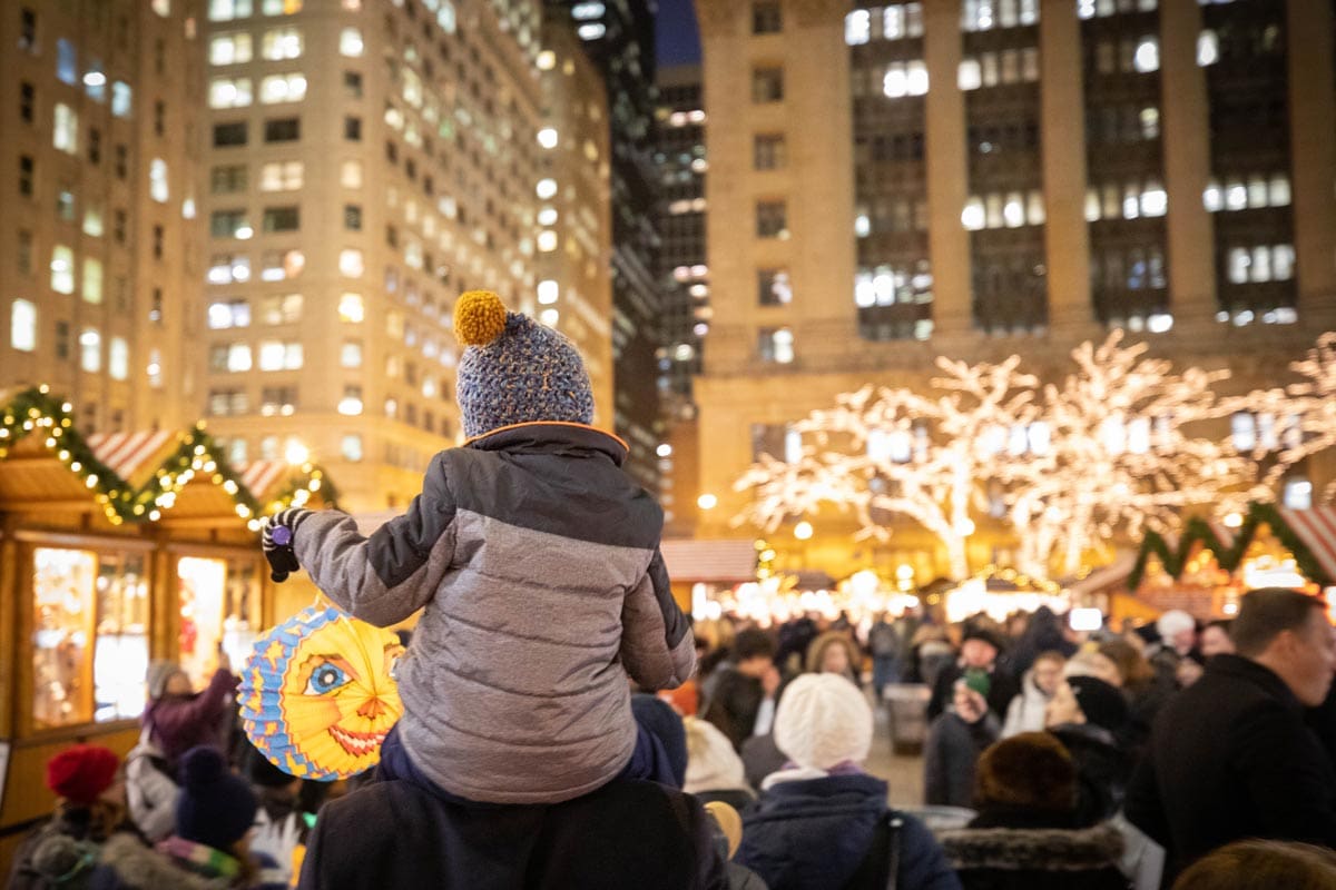 A young child sits atop the shoulder of an adult to take in a view of the lights and market sights at Christkindlmarket Chicago.