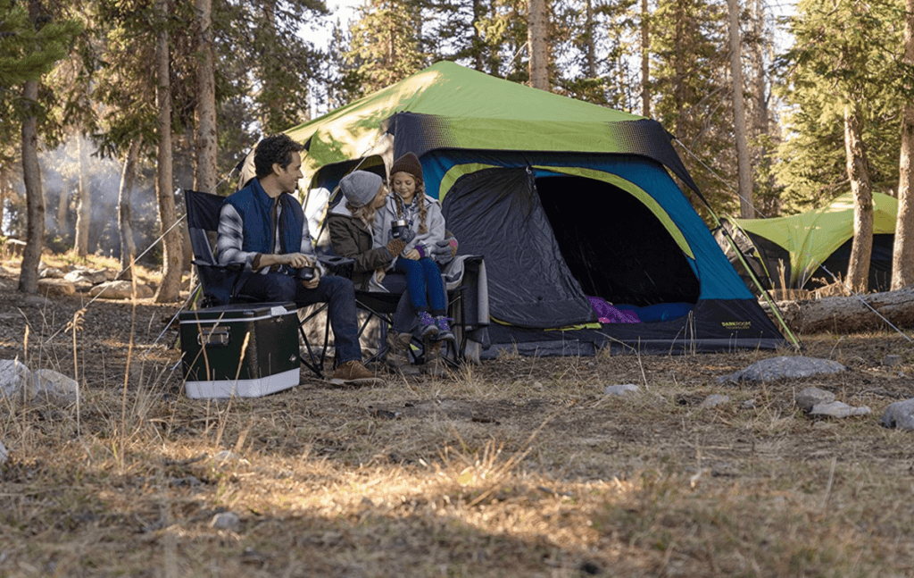 A family of three sits in front of the Coleman Cabin Tent, one of the best gifts for dads who travel, while enjoying a camping trip in the woods.