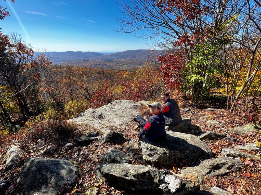 A dad and his son sit on a rock ledge overlooking a beautiful view of fall foliage near Pittsfield.