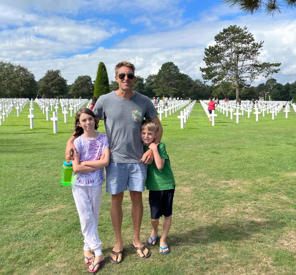 A dad and his two kids stand together at the Omaha Beach Cemetery in France, one of the best places to visit in France with kids.