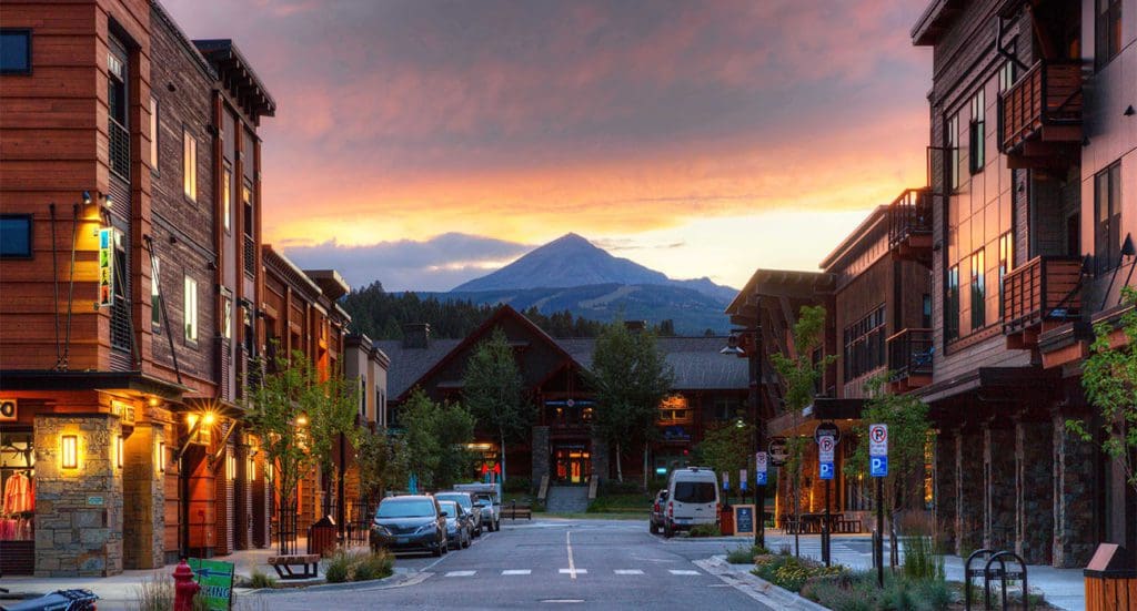 A view down a charming street in Big Sky, with mountains in the distance, at dusk.