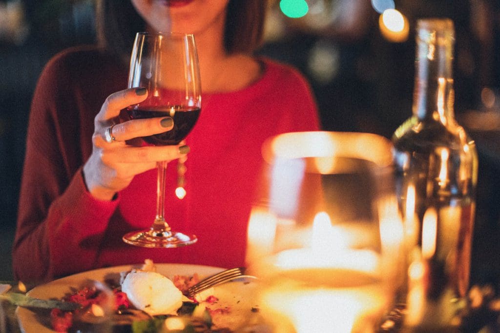 A close up of a candle lit dinner for two, with the woman's body in the background holding up a class of wine.
