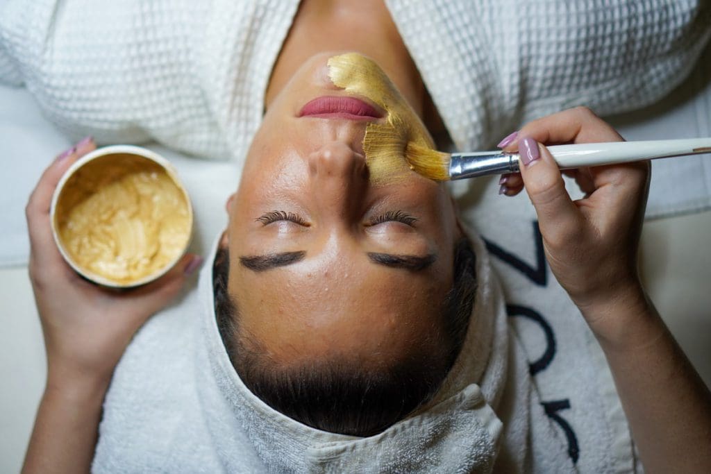 Hands reach out to apply a spa service to a woman's face.