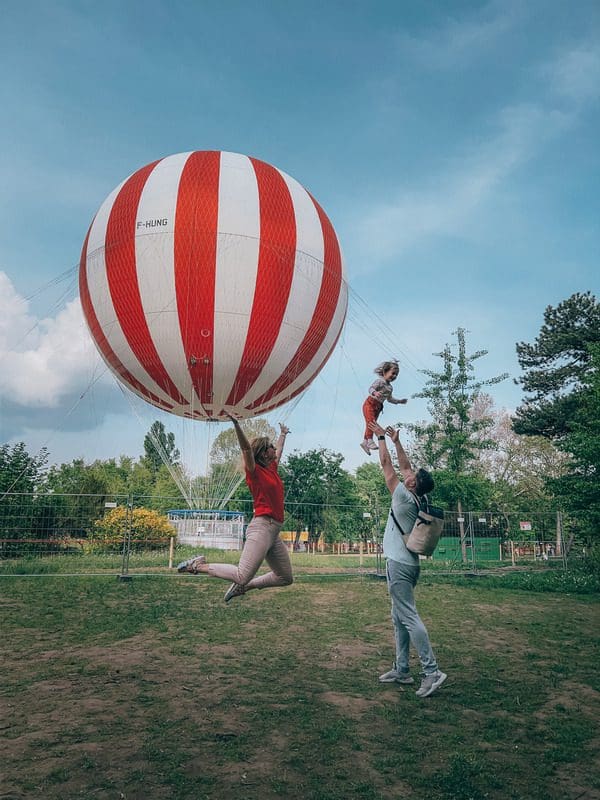 A family jumps for joy in front of a large red and white hot air ballon from BalloonFly in Budapest.