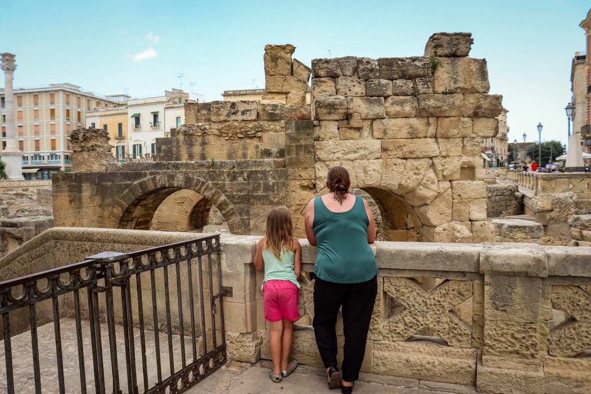 A mom and her young daughter stand together looking at Roman ruins in Lecce.