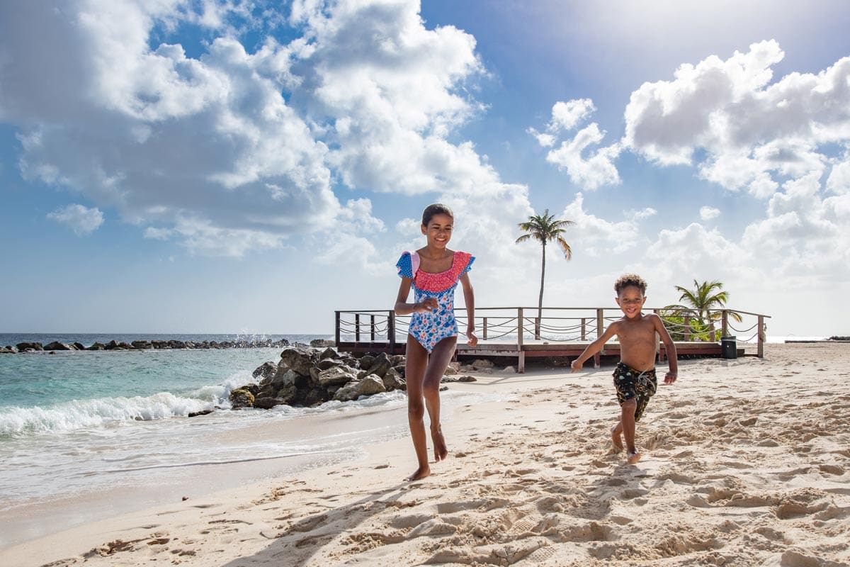 Two kids run across the beach on-site at Curaçao Marriott Beach Resort.
