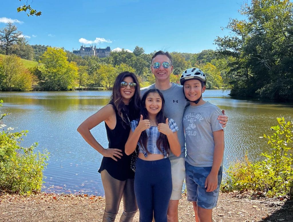 A family of four stands together with the Biltmore Estate in the distance.