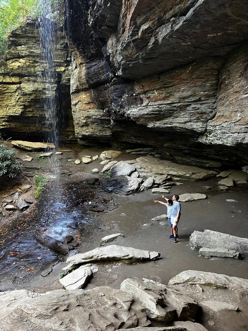 A dad and his young son enjoy a waterfall within Pisgah National Forest, while hiking near Asheville.