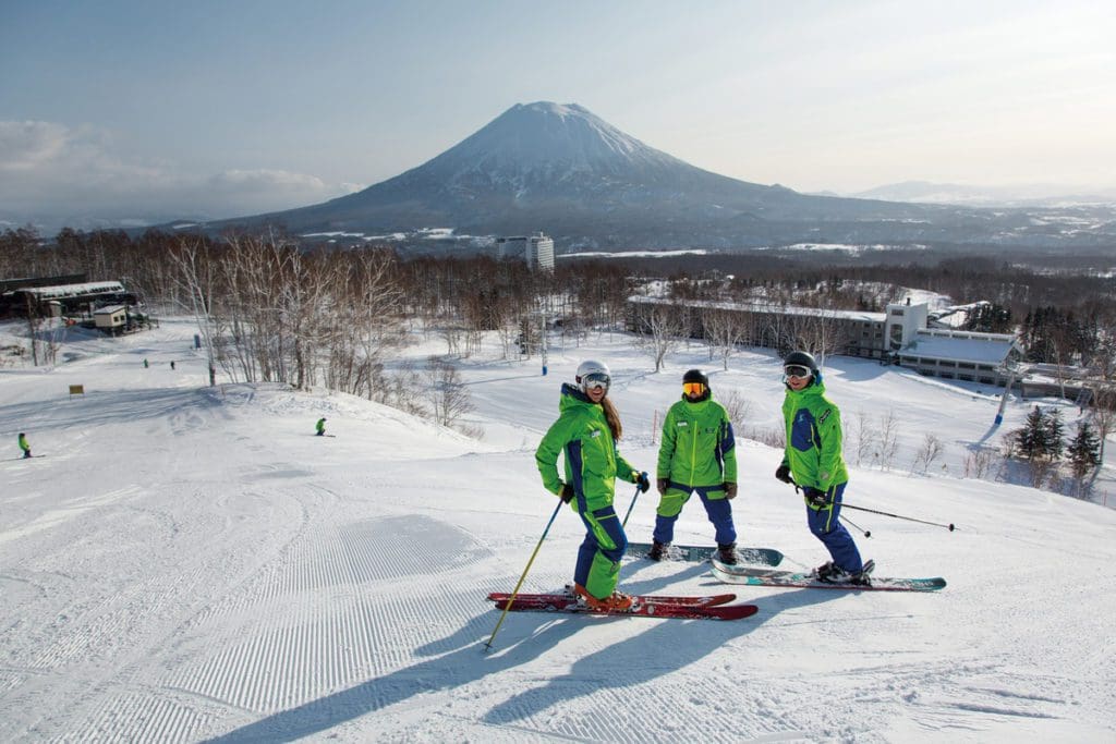 Three people on skis stand together at the top of a slope at Niseko United.