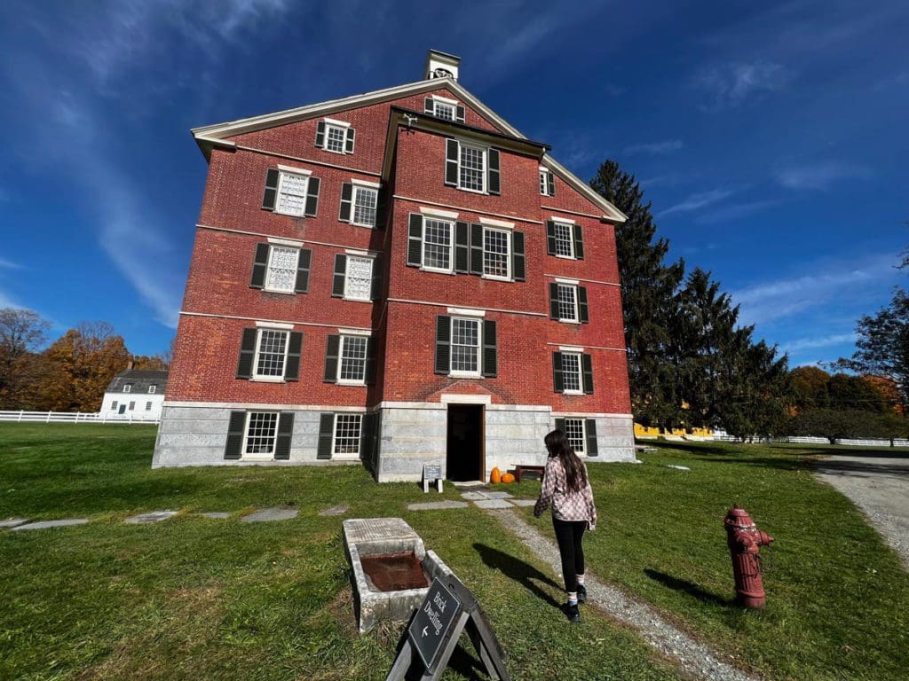 A girl walks toward the Brick Dwelling, a large brick building, at Hancock Shaker Village.