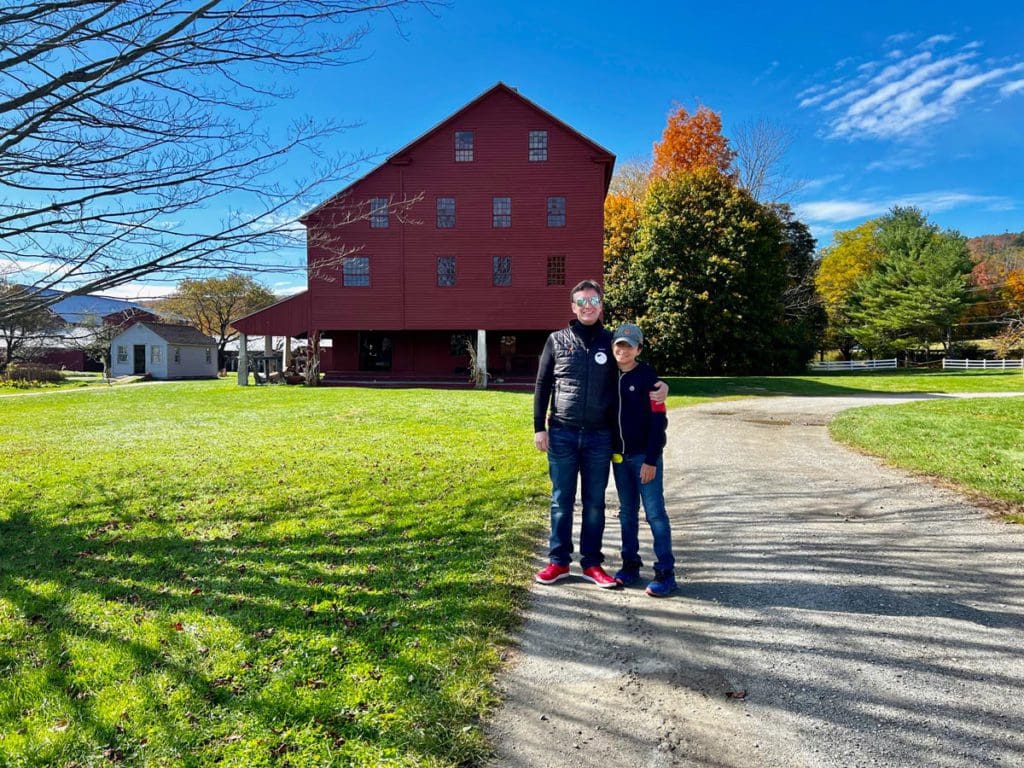 A dad and his son stand together outside a red building at Hancock Shaker Village, near Pittsfield, MA, one of the best places to visit for fall in New England with kids.