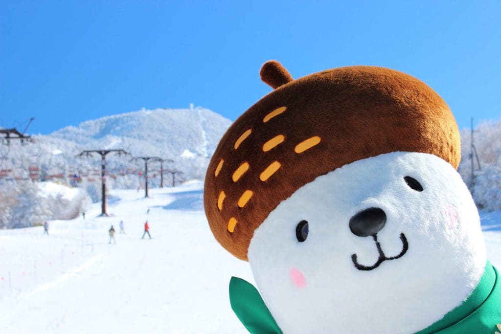 A ski mascot pokes its head into frame with alpine slopes in the distance at Shiga Kogen Mountain Resort.