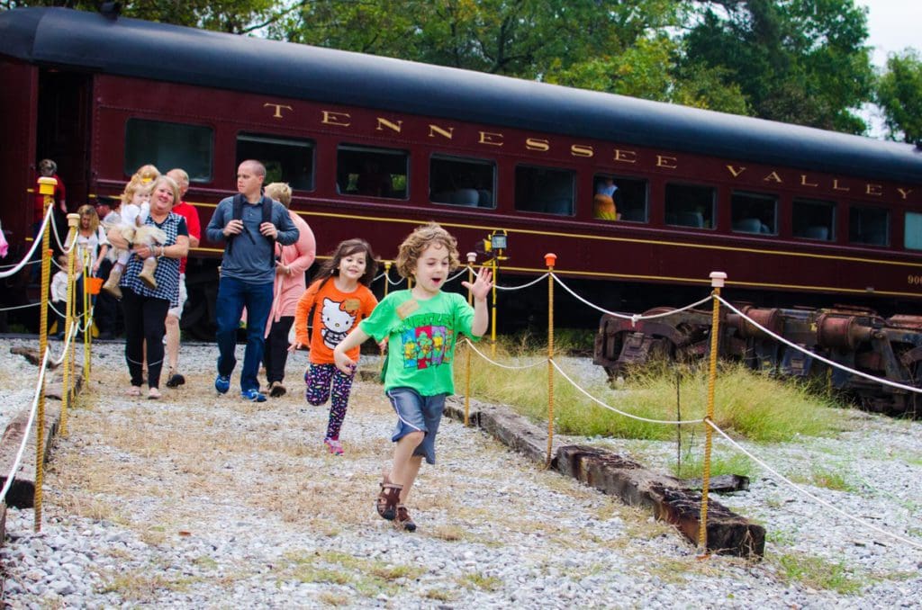 A conductor and several kids walk away from a train, part of the Tennessee Valley Railroad Museum.
