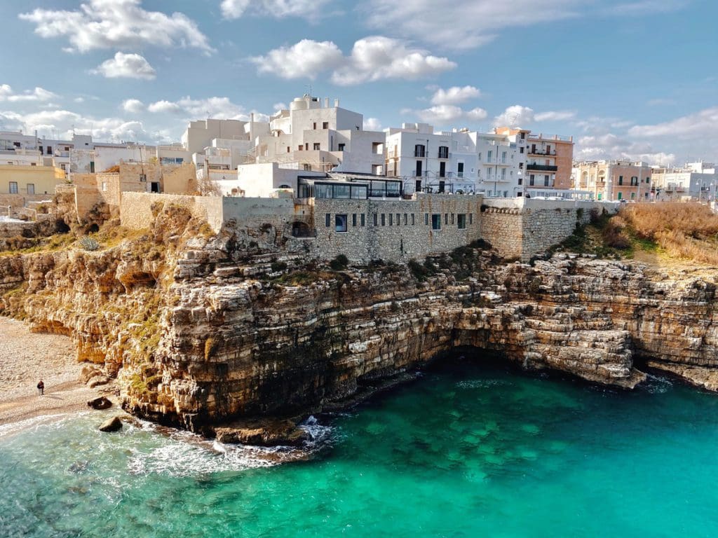 The old city walls of Polignano a Mare rising from the sea, with the ocean below.