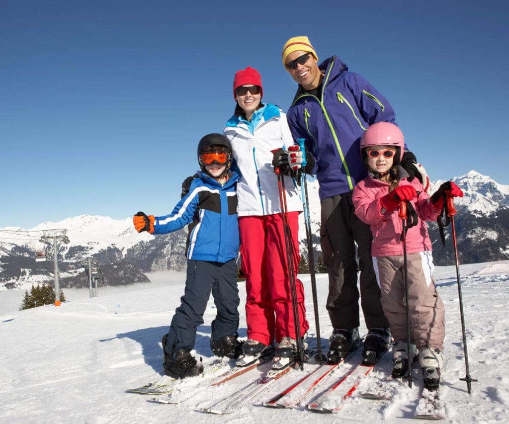 A family of four stands together on top of a mountain slope while skiing together.