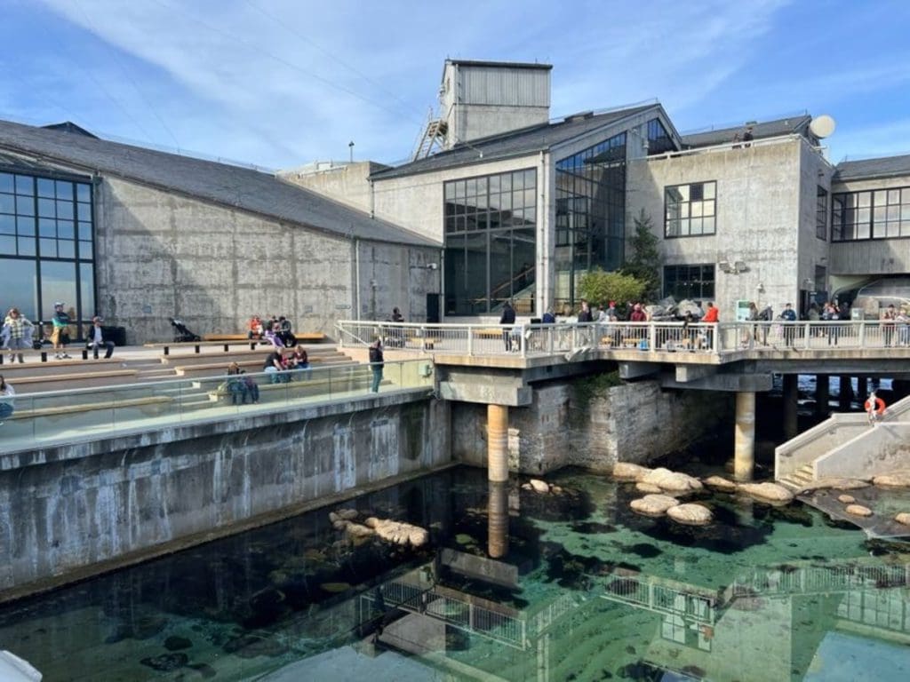 Several people meander a balcony area overlooking the ocean at Monterey Bay Aquarium.