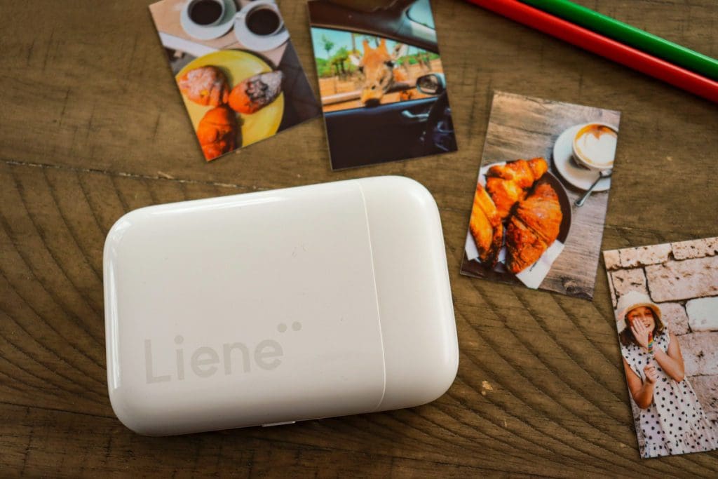 A Liene Pearl Portable Photo Printer near four printed pictures and two colored pencils.