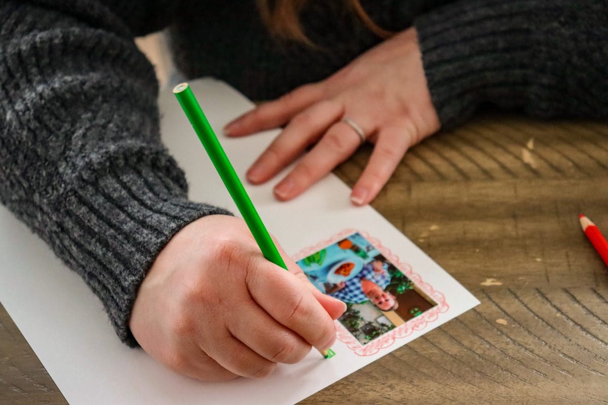A close up of a hand coloring a travel journal page with pictures.