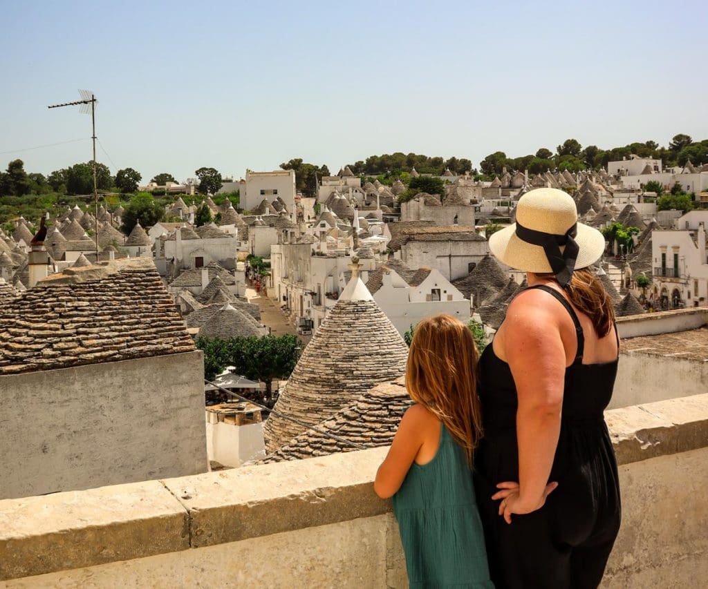 A mom and her young daughter stand together overlooking a scenic view of the traditional trulli of Alberobello, one of the best places to visit in Italy on a budget with kids. 