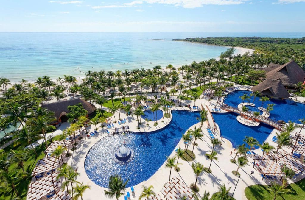 An aerial view of Barceló Maya Grand Resort, featuring large pools, swaying palm trees, and beautiful ocean front access.