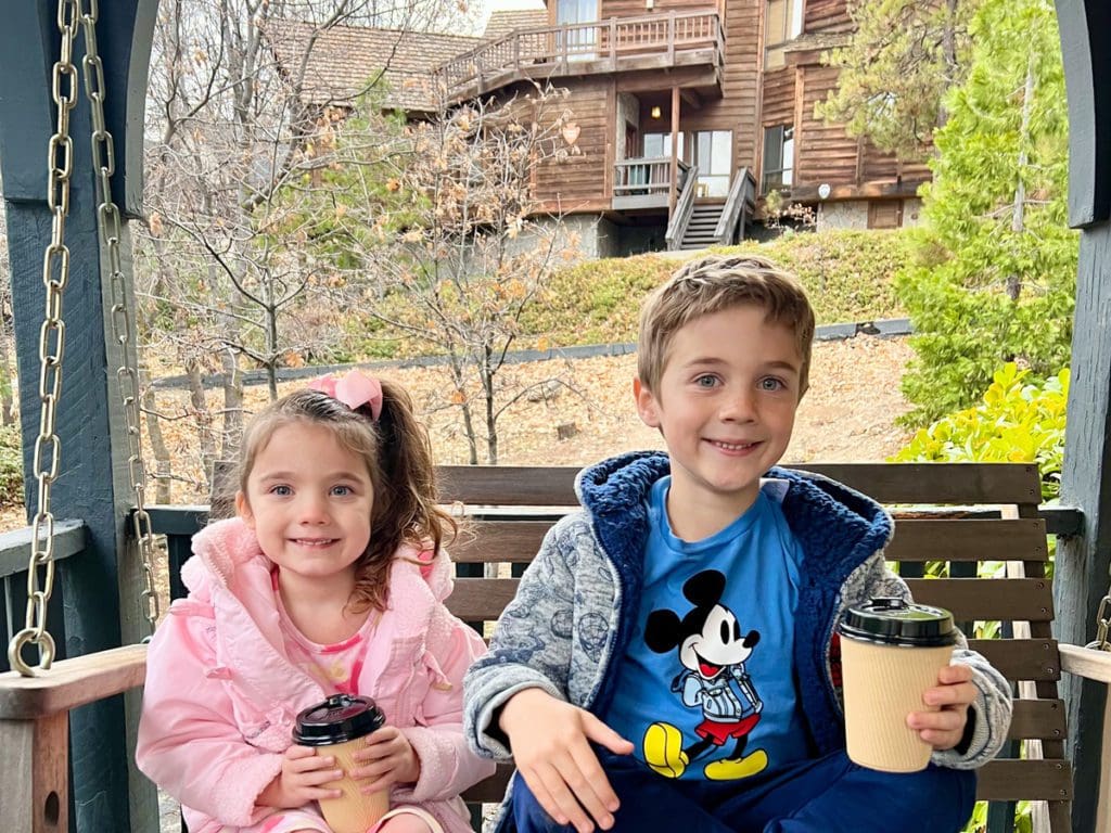 Two kids enjoy a cup of hot cocoa on a porch swing.