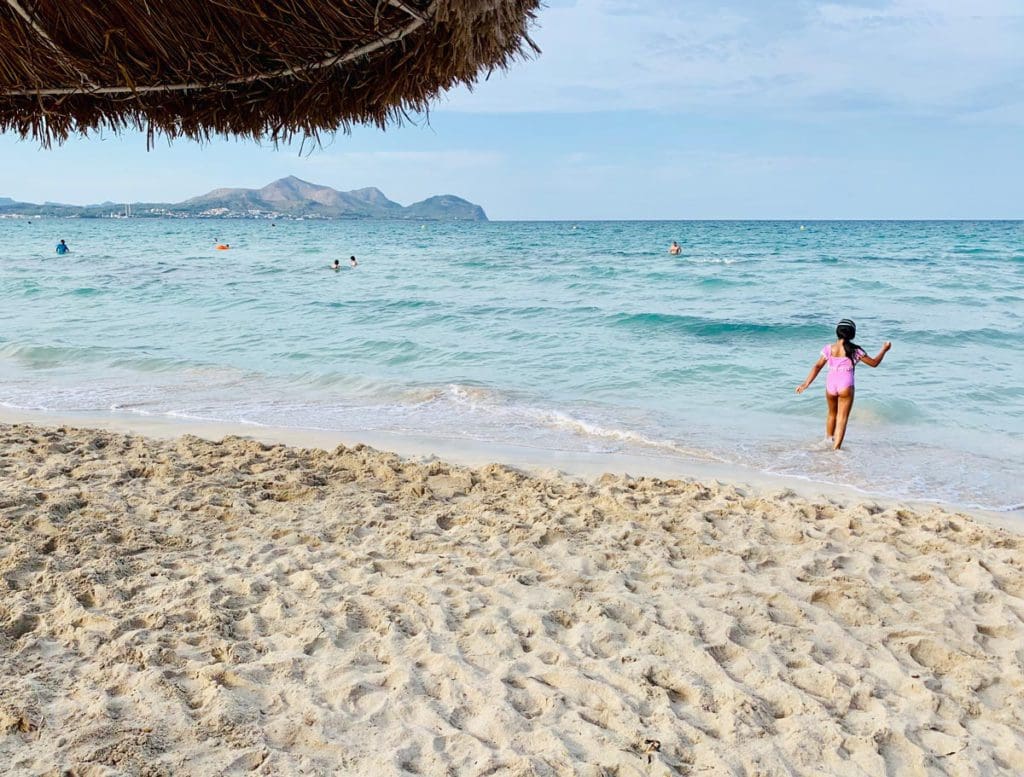 A young girl in a pink bathing suite wanders in the waves off-shore from a beach in Mallorca.