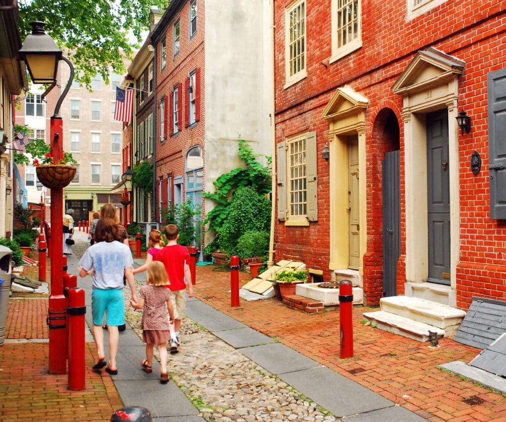 A family of three walks down a historic street in Philadelphia together. It's one of the best places for an East Coast road trip for families!