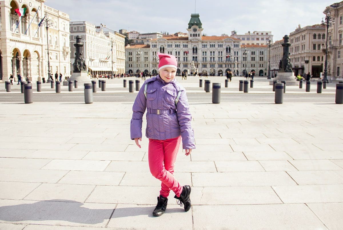 A young girl stands in a piazza in Trieste, one of the best neighborhoods to stay in Rome with kids.