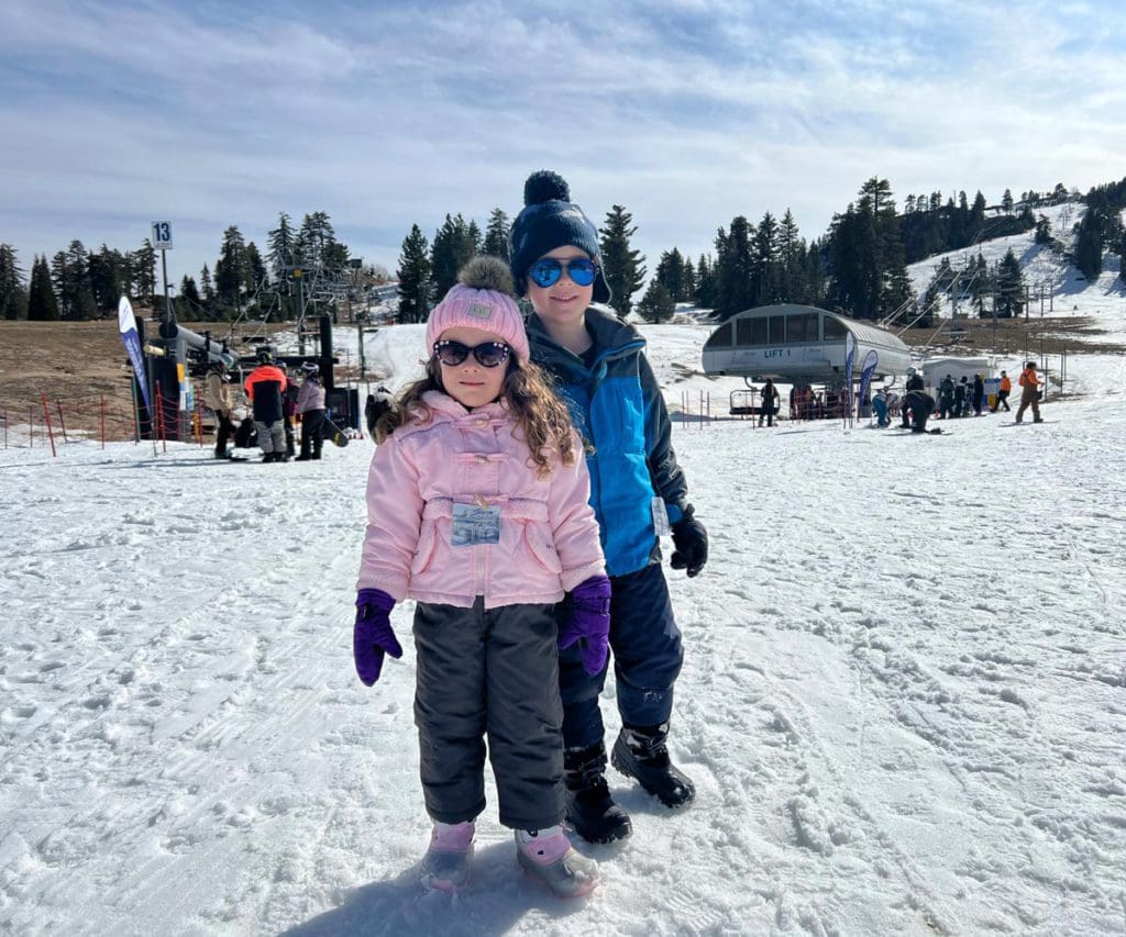 Two kids stand together in the snow during a trip to UCLA Arrowhead Lodge.