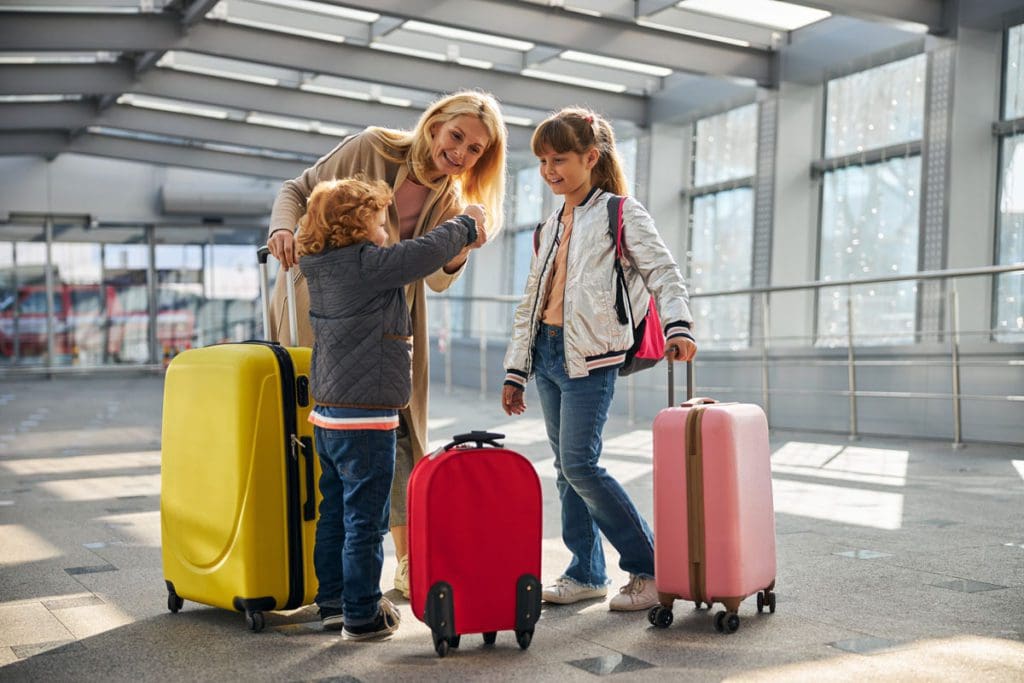 A mom and her two kids stand with their carry-on luggage at the airport, knowing the baggage allowance is critical to understanding the Delta Airlines policies for kids.