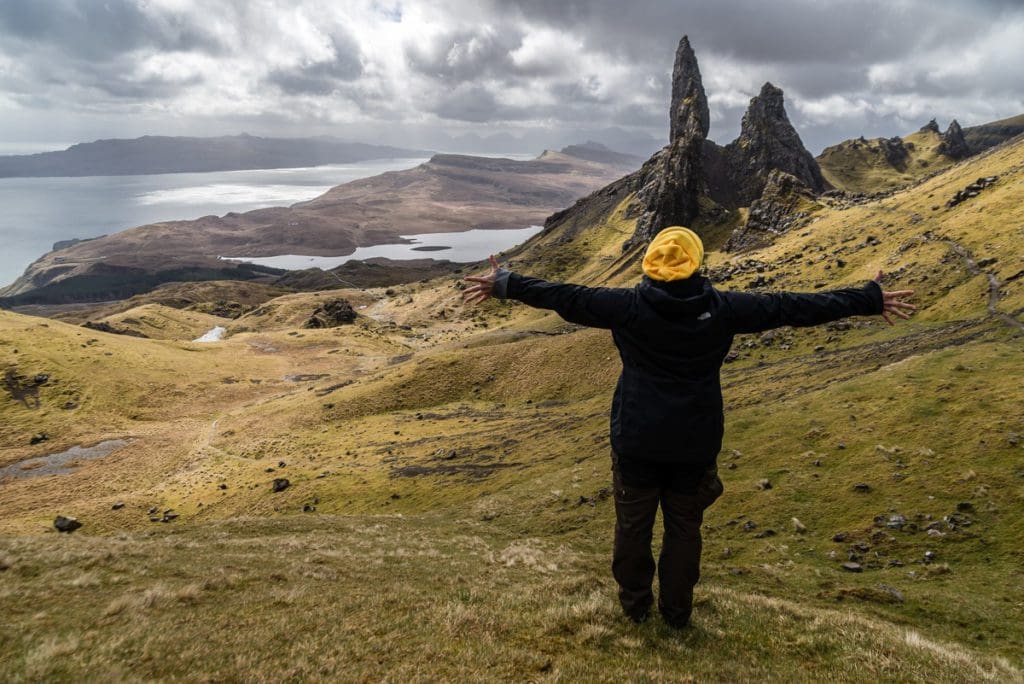 A young woman opens her arms wide to a scenic area of Scotland, one of the top places in travel in 2023 with kids.