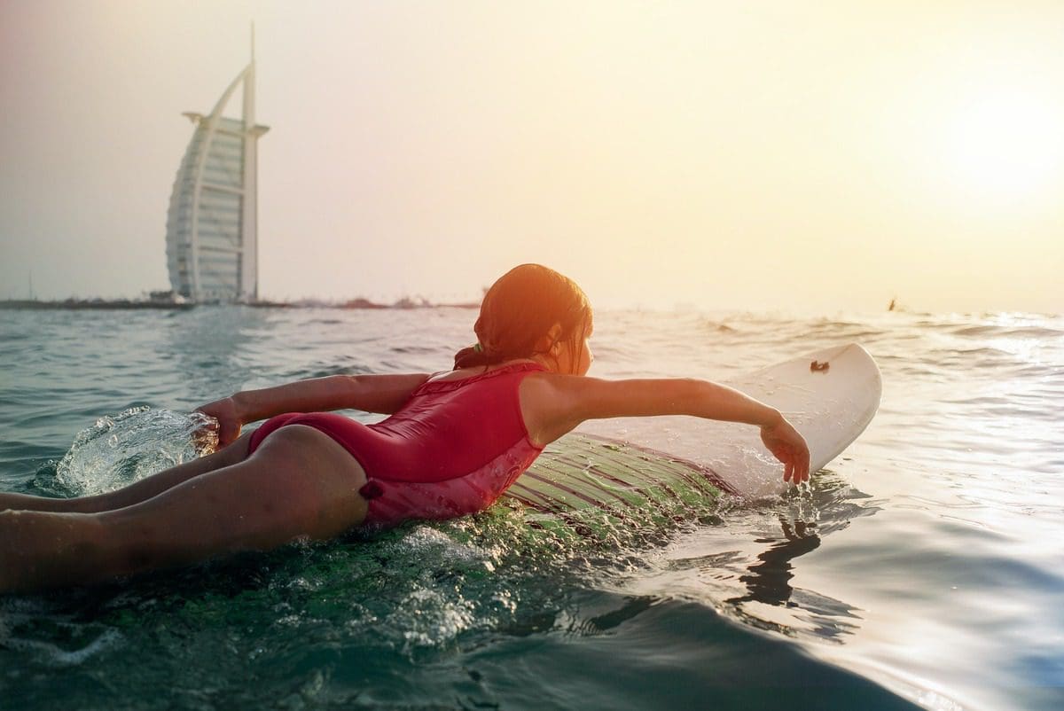 A young girl paddles on a surf board with the Burj Khalifa in the background.