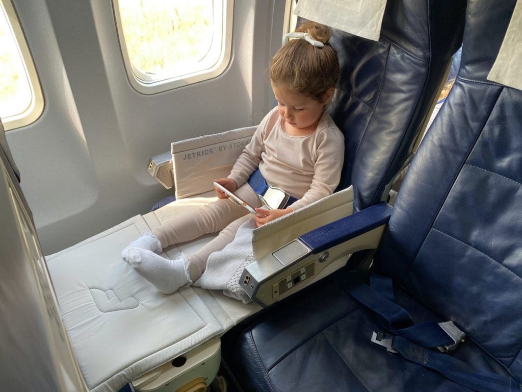 A young girl sits on a plane in her JetKids by Stokke, while traveling one of the best airlines for kids.