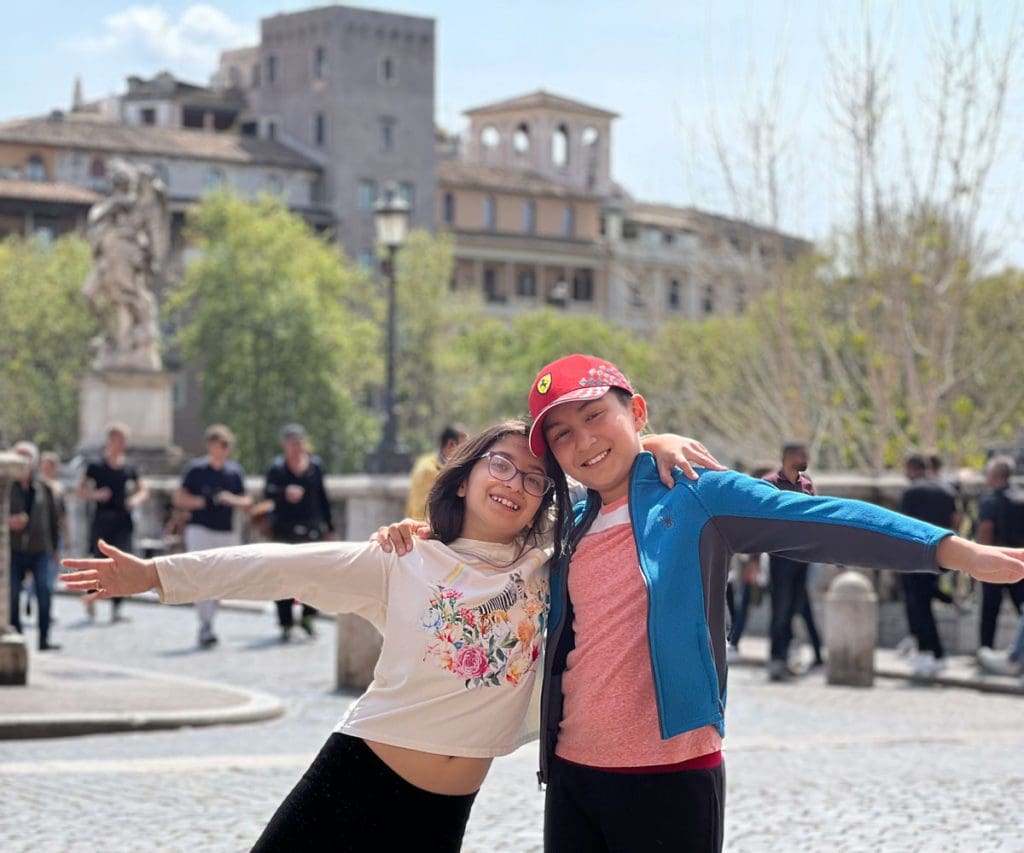 Two kids stand together outside the Vatican, while exploring Rome as a family.