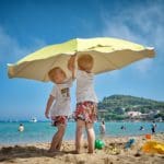 Two young boys play under a sun umbrella, while traveling with their family.