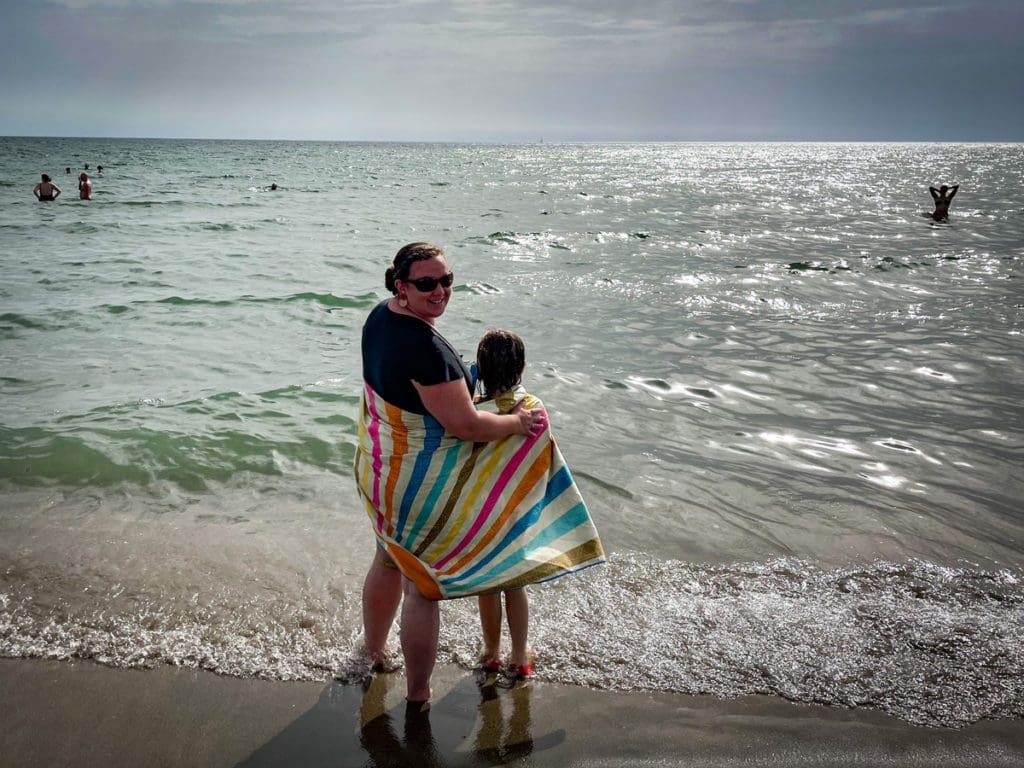 A mom and her daughter wrapped in an Onda beach towel on a beach in Italy.