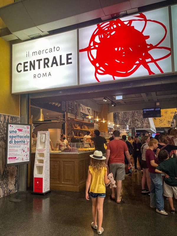 A young girl walks into Il Mercato Centrale Roma, a trendy food hall in Termini Station in Rome, this is one of the best neighborhoods to stay in Rome with kids.
