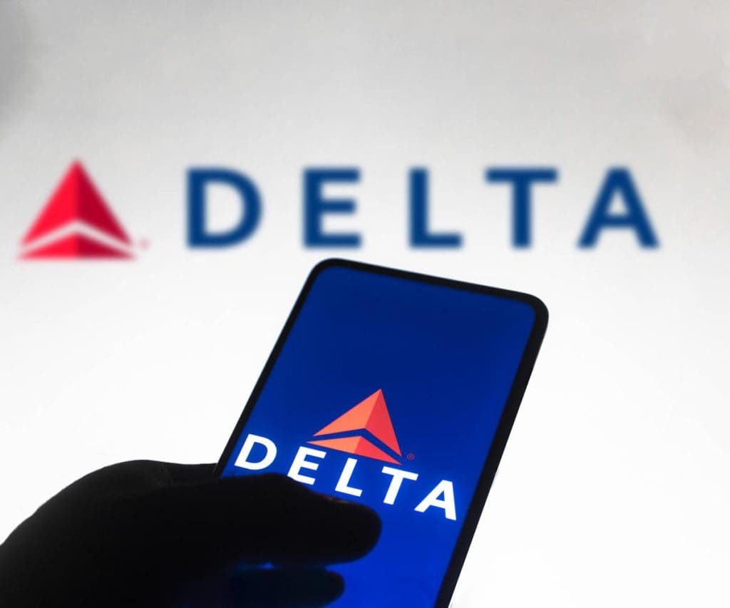 A hand navigates the Delta Airlines app with the Delta logo in the background.