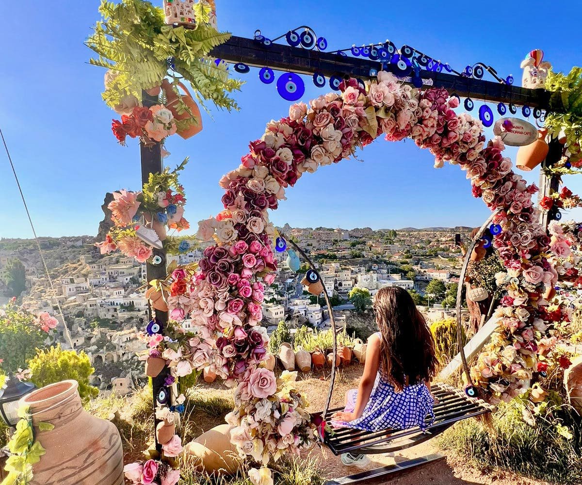 A young girl sits on a flower-laden swing overlooking a city in Turkey.