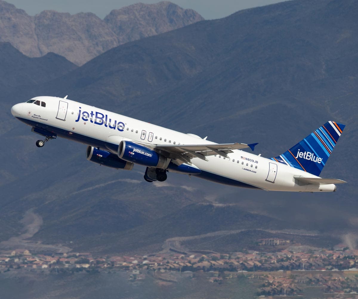 A Jet Blue carrier takes off from an airport in the mountains.