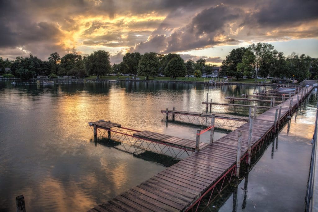 A setting sun over the pier on the lake in Skaneateles, NY, as part of the Finger Lakes region, one of the best affordable summer vacations in the United States with kids.