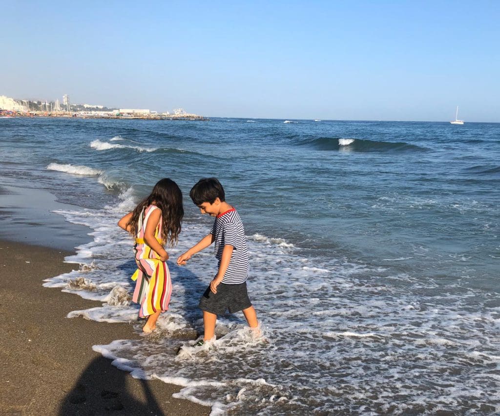 Two young kids splash in the surf along a beach in Marbella.