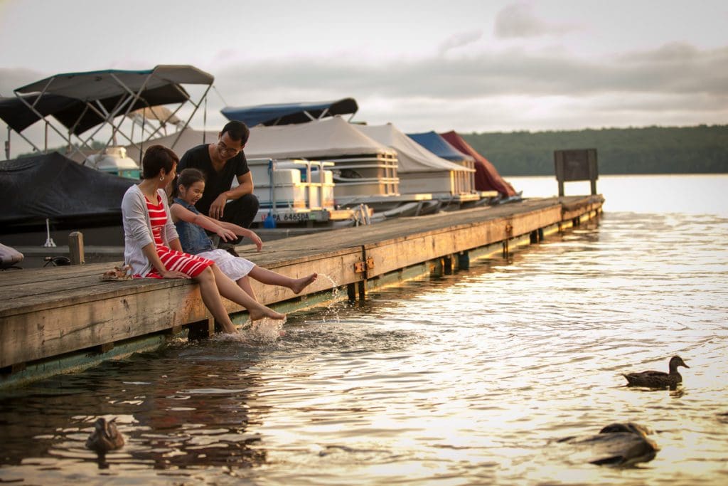 A family enjoys feeding the ducks from a dock at sunset on Lake Wallenpaupack in the Pocono Mountains, one of the most affordable destinations in the US for families.