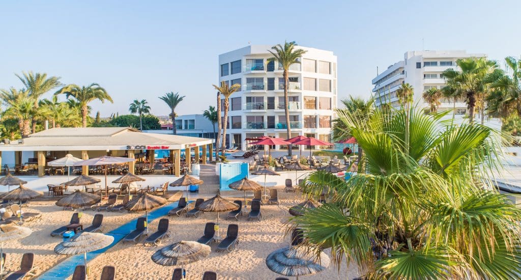 Beach loungers in the sand, with resort buildings in the distance, at Adams Beach Hotel.