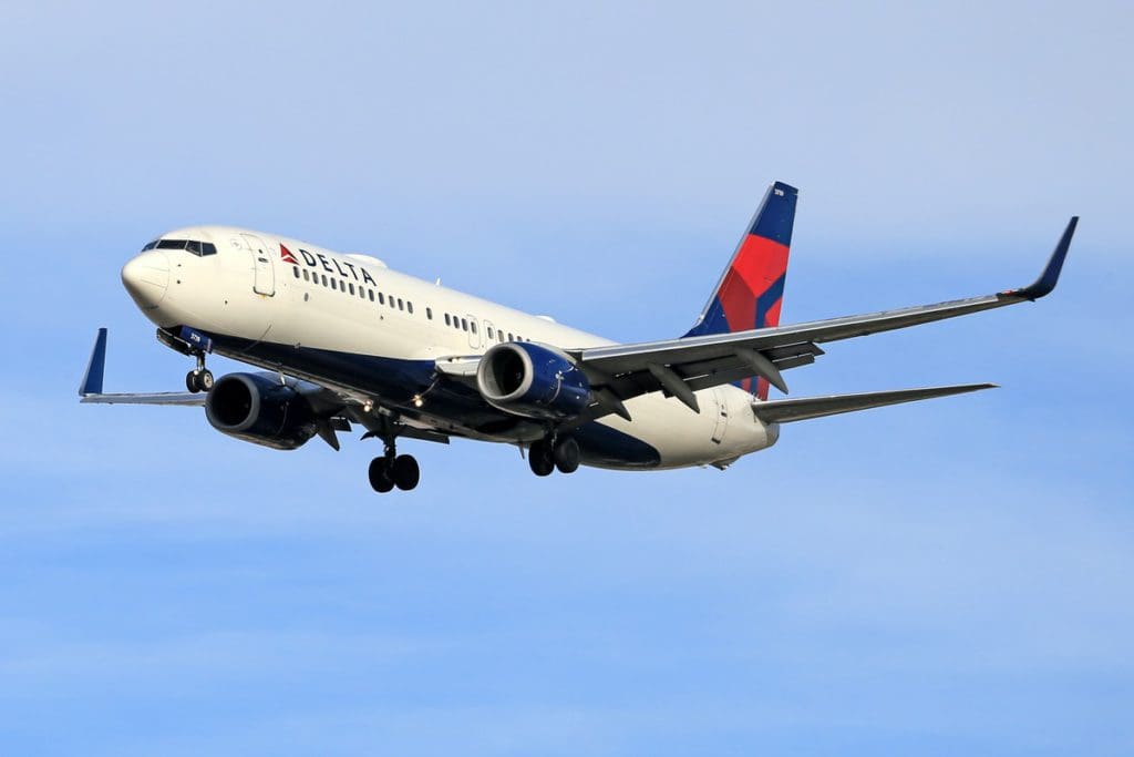 A Delta Airlines plane soars through a clear blue sky. 