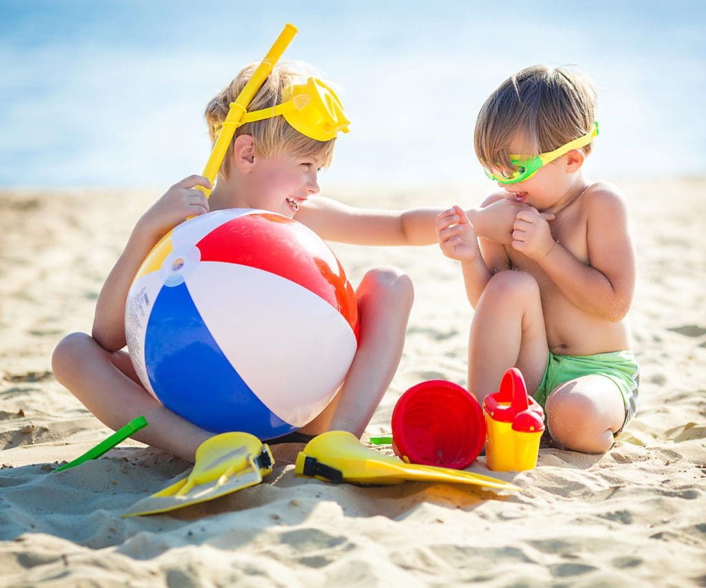 Two kids playing on the beach together with beach toys.