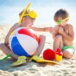 Two kids playing on the beach together with beach toys.