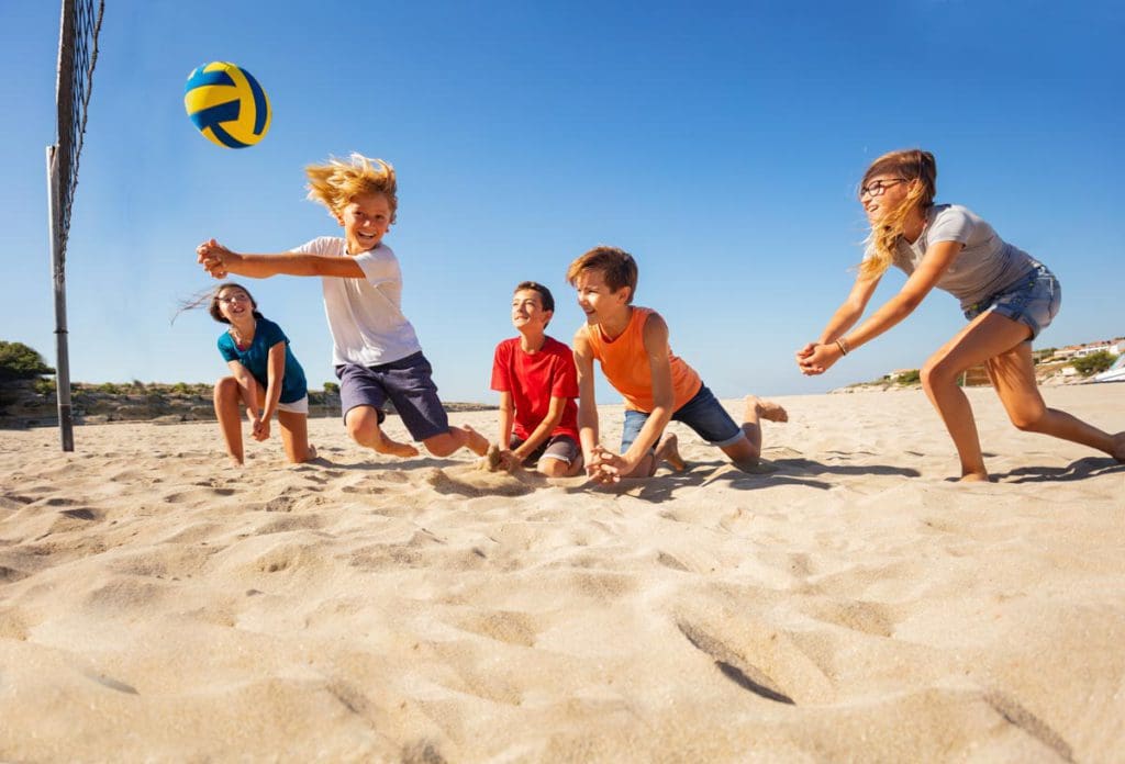 Five kids play beach volley ball together in the sun.